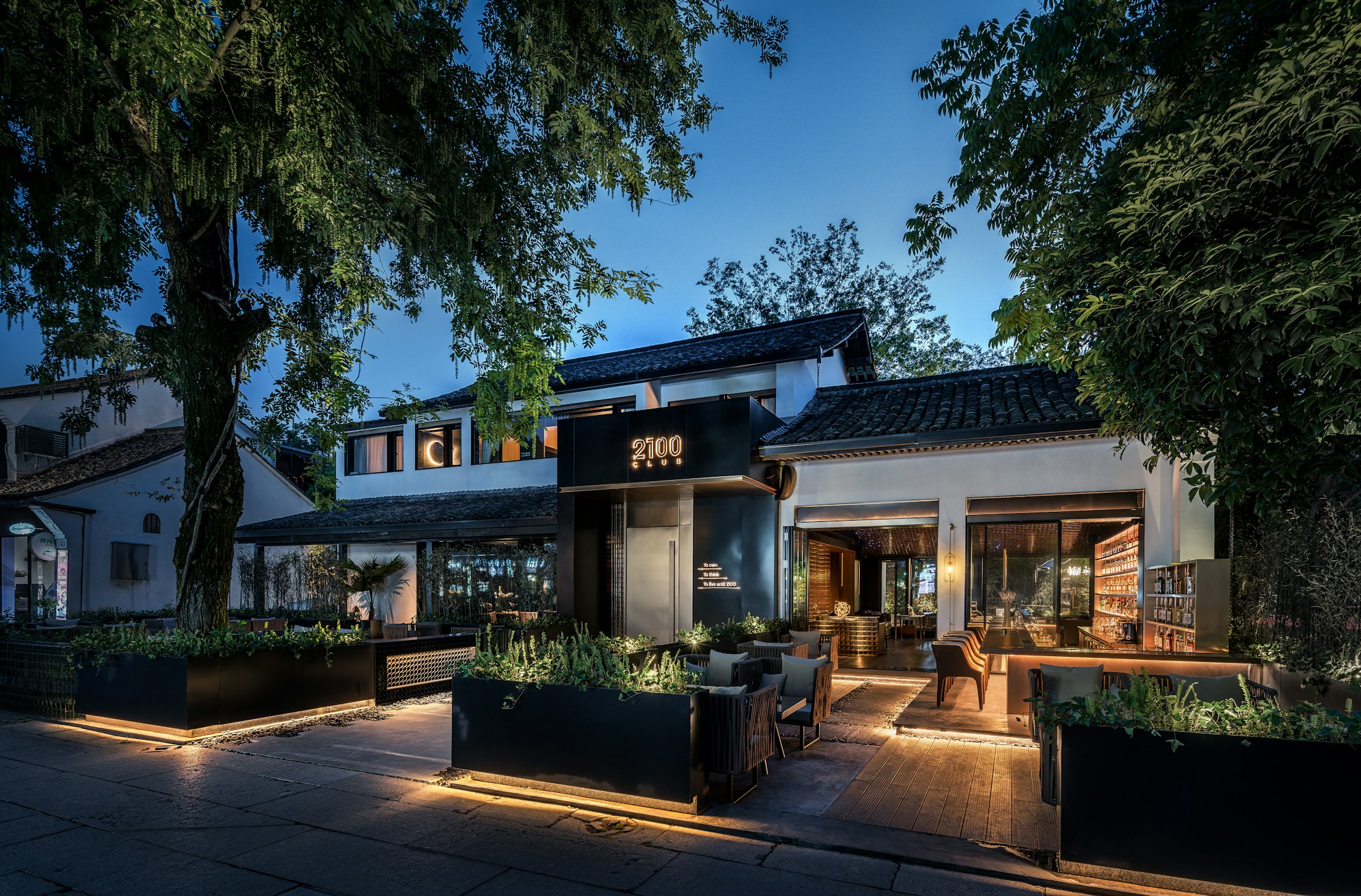 Occupied restaurant storefront lit at dusk, with patio seating out front